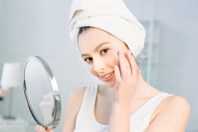 A woman smiling while checking her skin in a hand mirror.